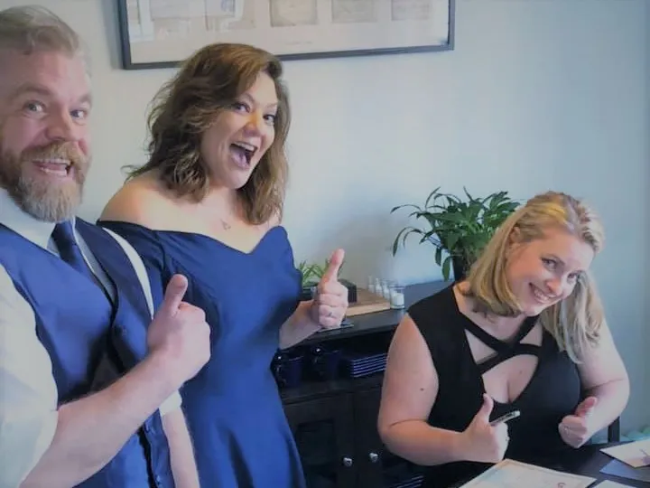 Newlyweds and friend grinning with thumbs up