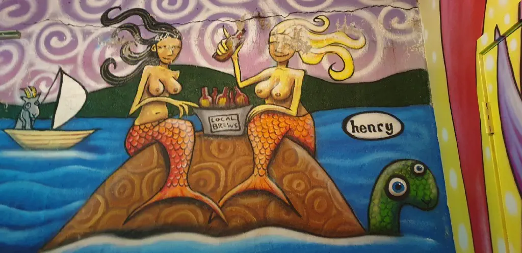 Wall art of buxom mermaids drinking beer on a turtle&rsquo;s shell while a goat in a boat watches