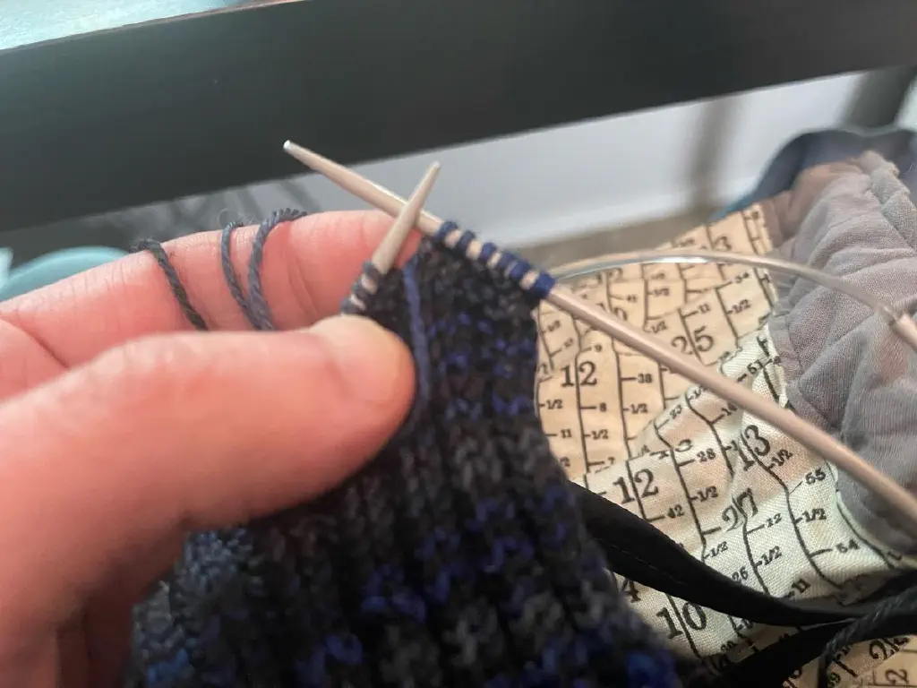 Close-up of hand holding a knitted sock in progress, six stitches into a new row