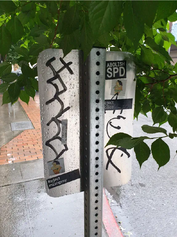on the back of a &ldquo;no parking&rdquo; sign, stickers that read &ldquo;ABOLISH SPD&rdquo;, &ldquo;Reject Police&rdquo;, &ldquo;Reject Misogyny&rdquo; , and &ldquo;TRUMP IS GOING TO FUCK US ALL&rdquo;