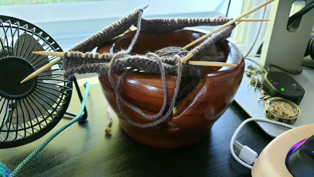 A few rows of knitted brown yarn with double pointed needles on wooden bowl