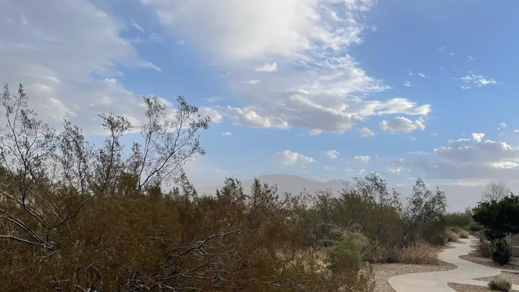 Desert brush scene under clouds scattered across a crystal blue sky; mountains in the near horizon are heavily obscured by ground-level haze