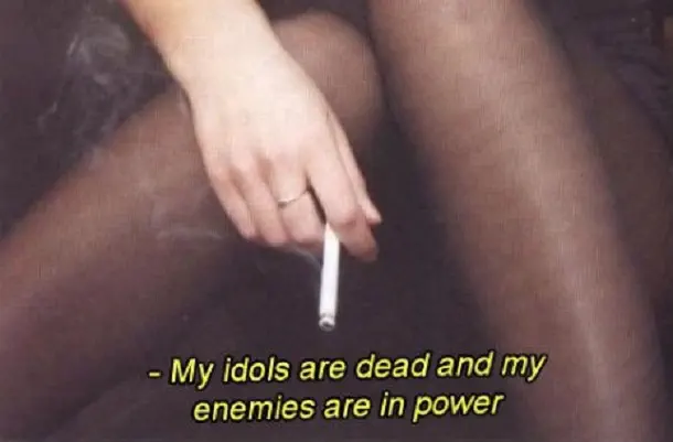 hand draped over stockinged legs, holding a cigarette; caption reads &ldquo;My idols are dead and my enemies are in power&rdquo;