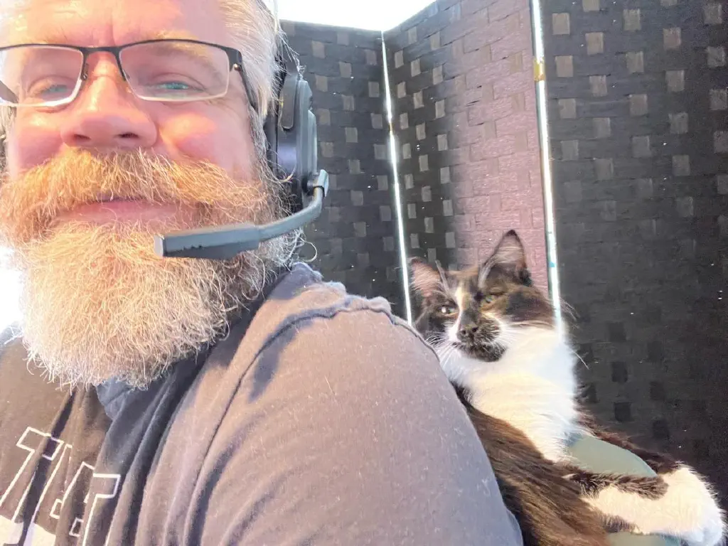 Selfie of beardy dude with cat wedged between dude’s back and office chair. 