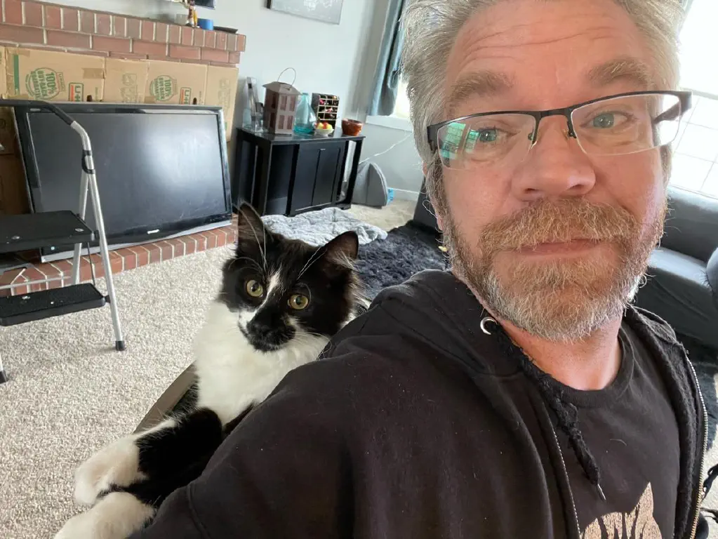 Scruffy dude with cat comfortable wedged between the chair and the dude’s back. 