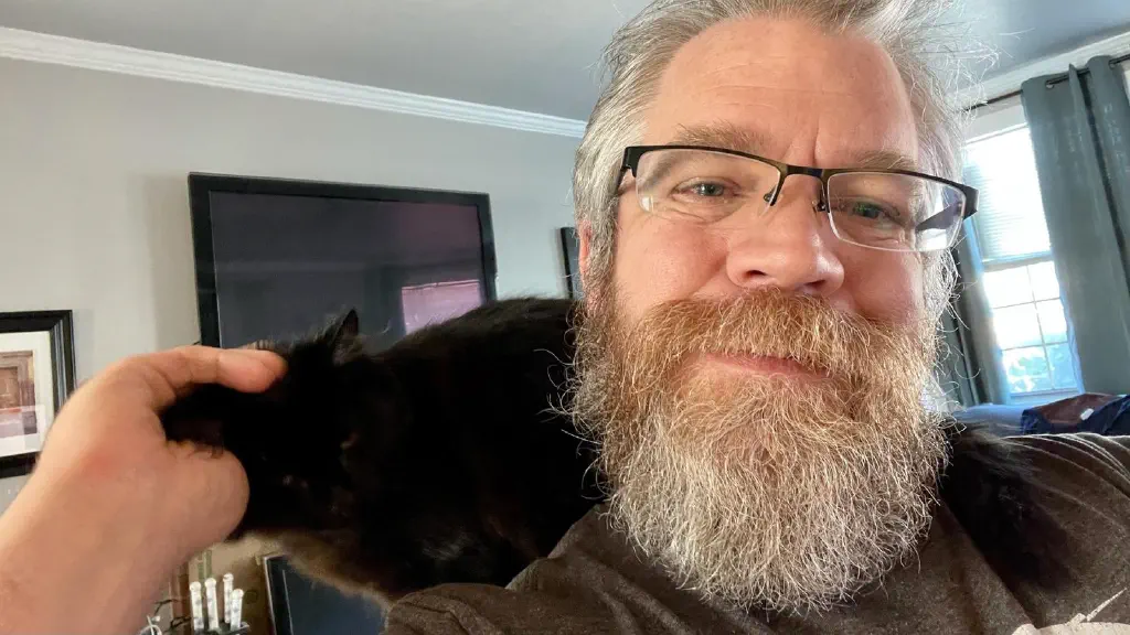 Beardy dude selfie with black kitten on shoulder getting ear skritches