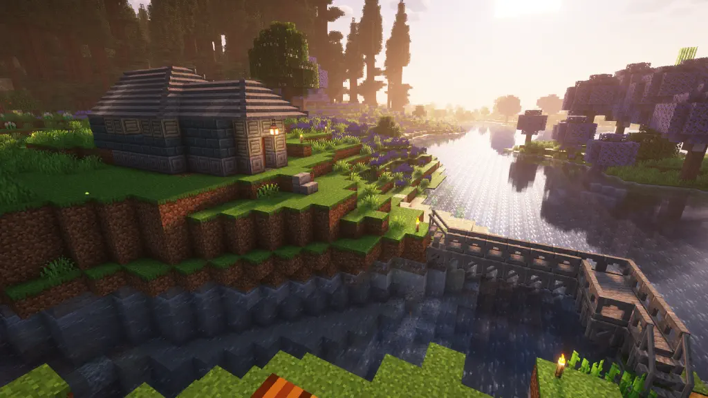 A stone bridge leads across the mouth of a river to a stone house on a hill with woods behind it; the house is assembled from an orderly combination of colors and patterned blocks; the roof is more angled and looks more like an actual roof than what is found in vanilla Minecraft