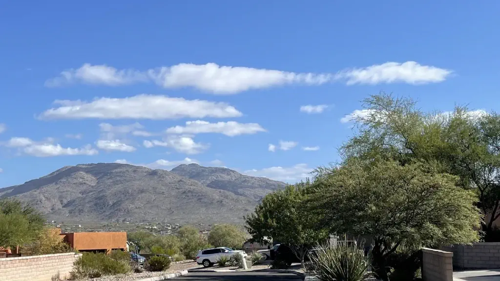 A few fluffy clouds against blue sky, casting scattered shadows on a couple desert mountains