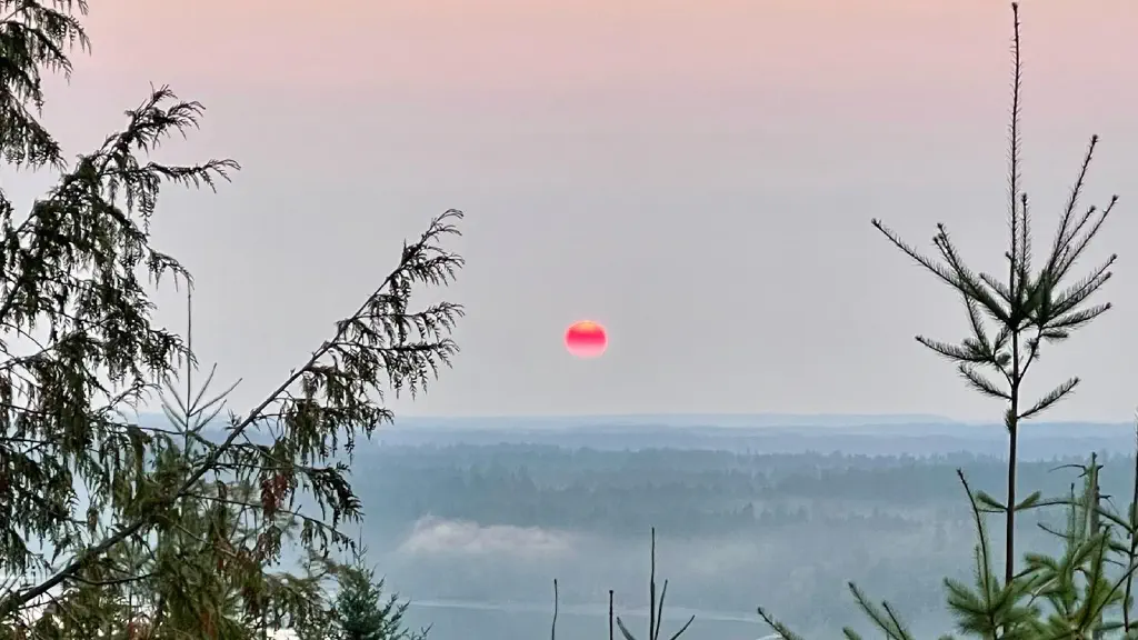 Very red sun rising over wooded hills. 