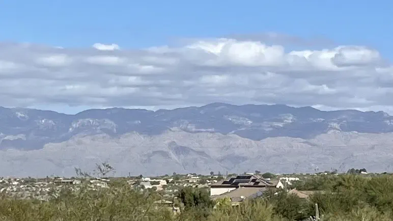 A layer of clouds low enough that you can see blue sky above them, casting their shadow on desert mountains