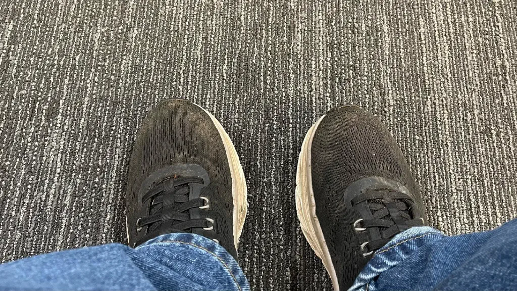 View from above of my dirty sneakers resting on a stripes beige waiting room carpet