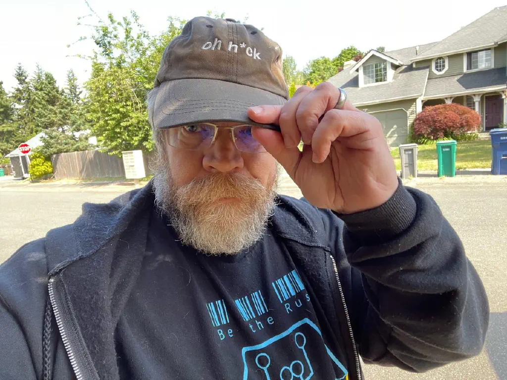 Beardy dude wearing a faded black cap printed with “oh h*ck” in white