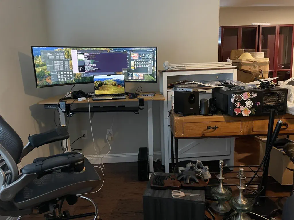 Desktop workspace in disarray, with laptop display extended to an ultrawide monitor, and a PC tower nearby on its side.