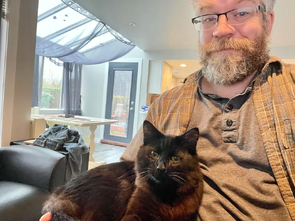 Happy black cat resting in the arm of an amused beardy dude
