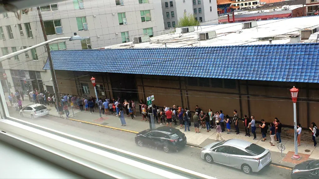A line of people across the street waiting to enter a restaurant