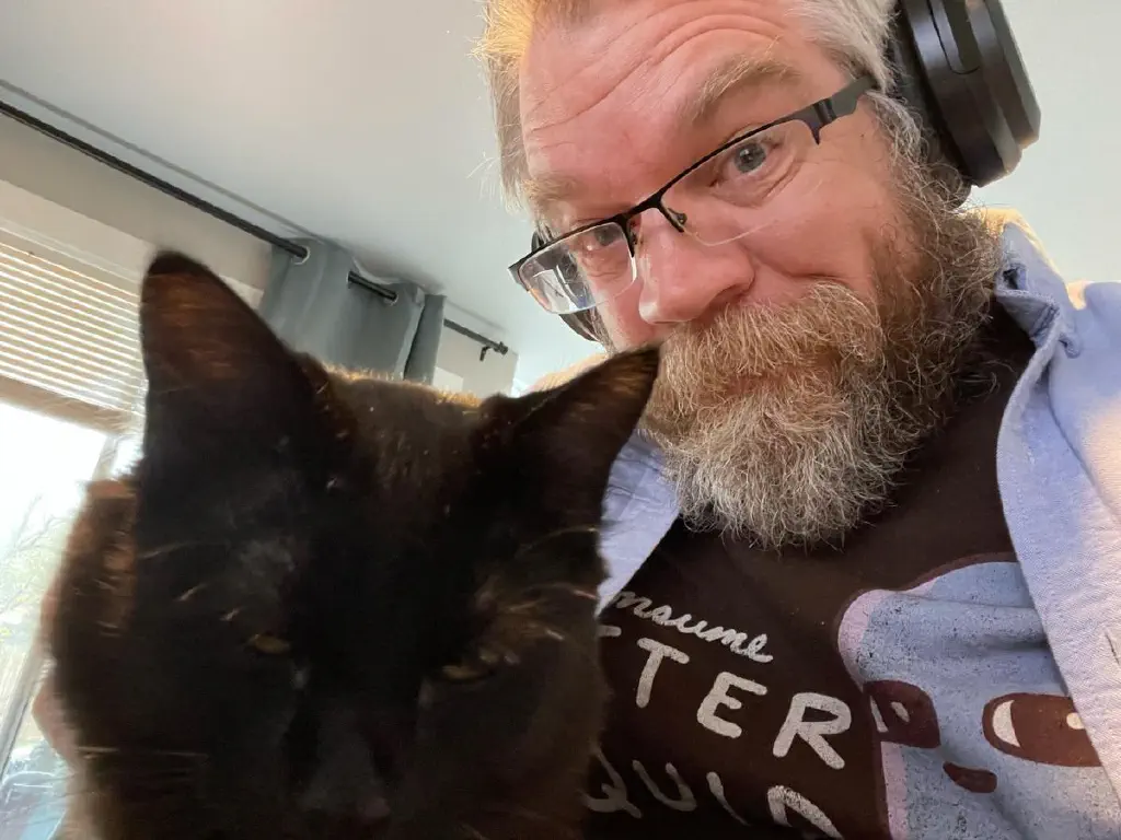 Selfie of beardy dude happily scritching black kitty