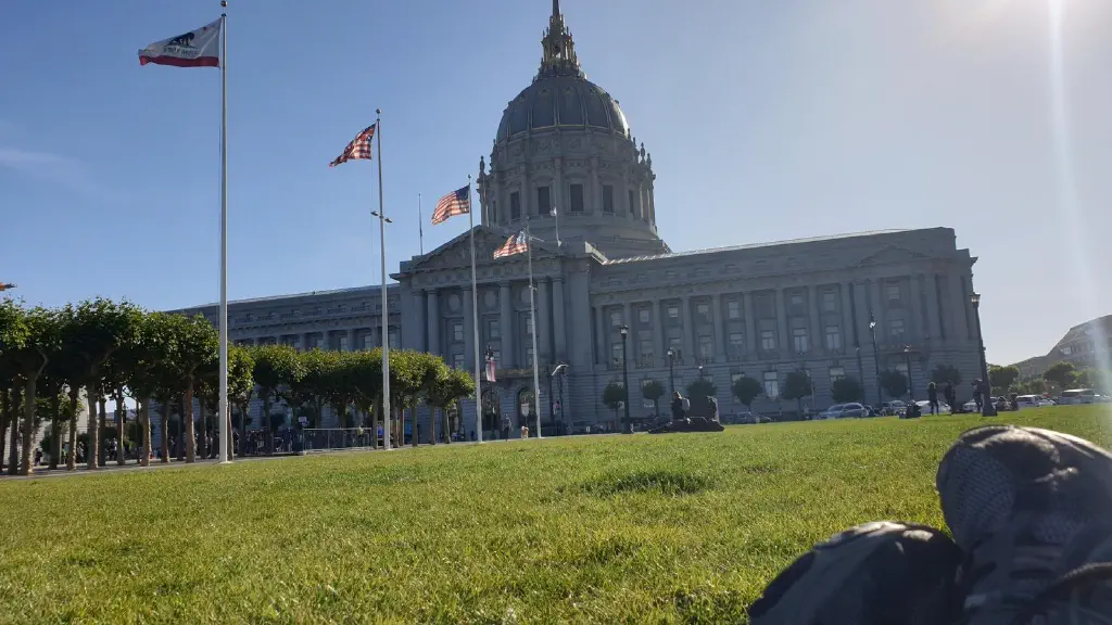Foreground: feet crossed on grass field. Background: San Francisco City Hall under sunny sky