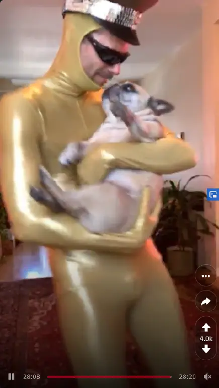 mustachioed man in shades, latex bodysuit, and hat, holding french bulldog