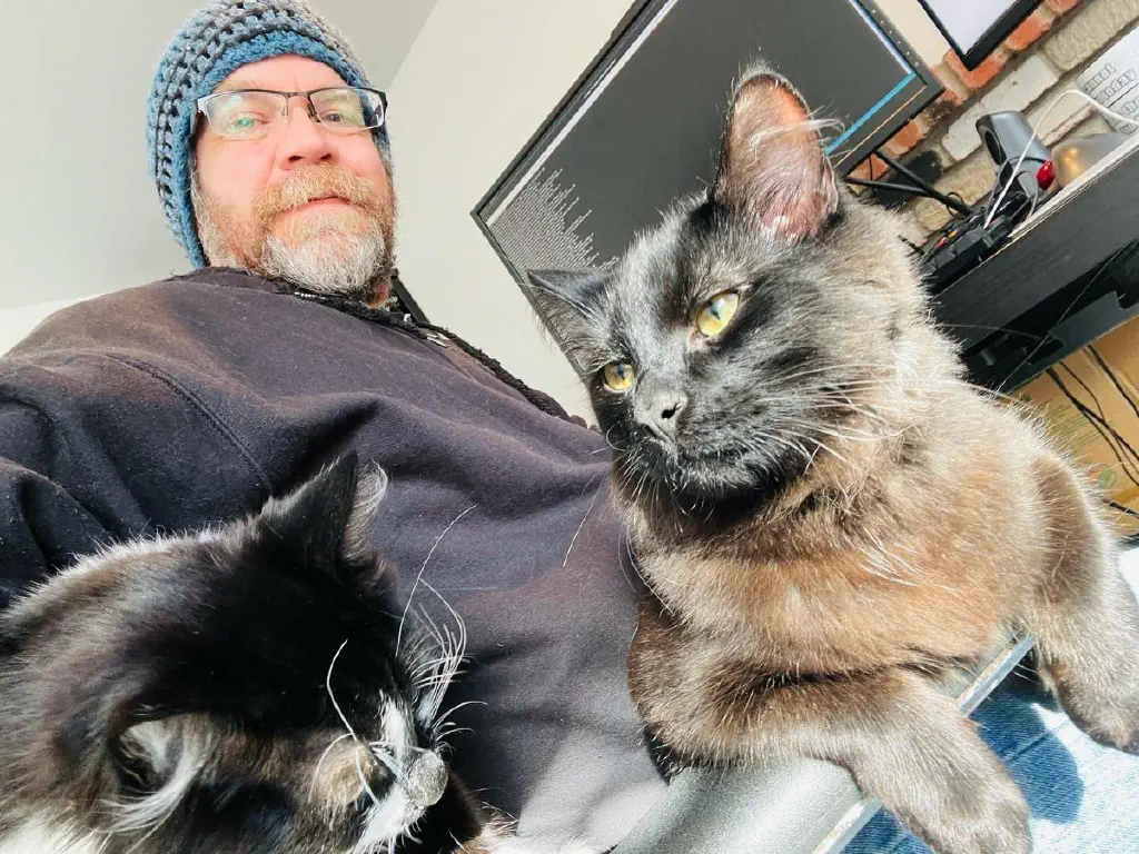 Beardy dude with cat in lap and another cat resting behind him