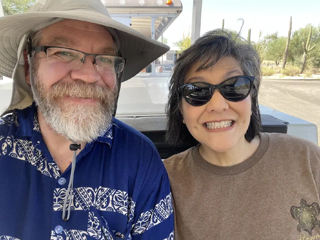 Beardy dude with sun hat and woman with short dark hair sunglasses both smiling big for the camera
