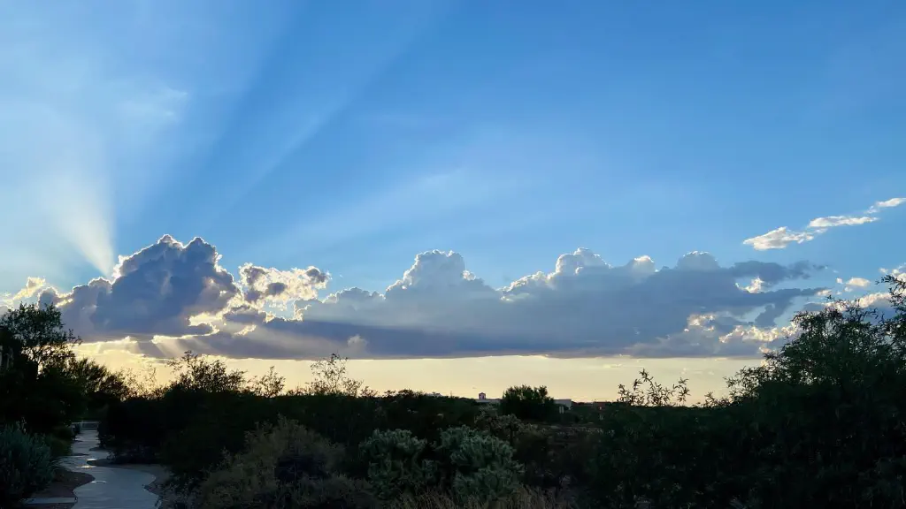 Rays of sunshine streaming past fluffy clouds obscuring the sun in an otherwise blue sky