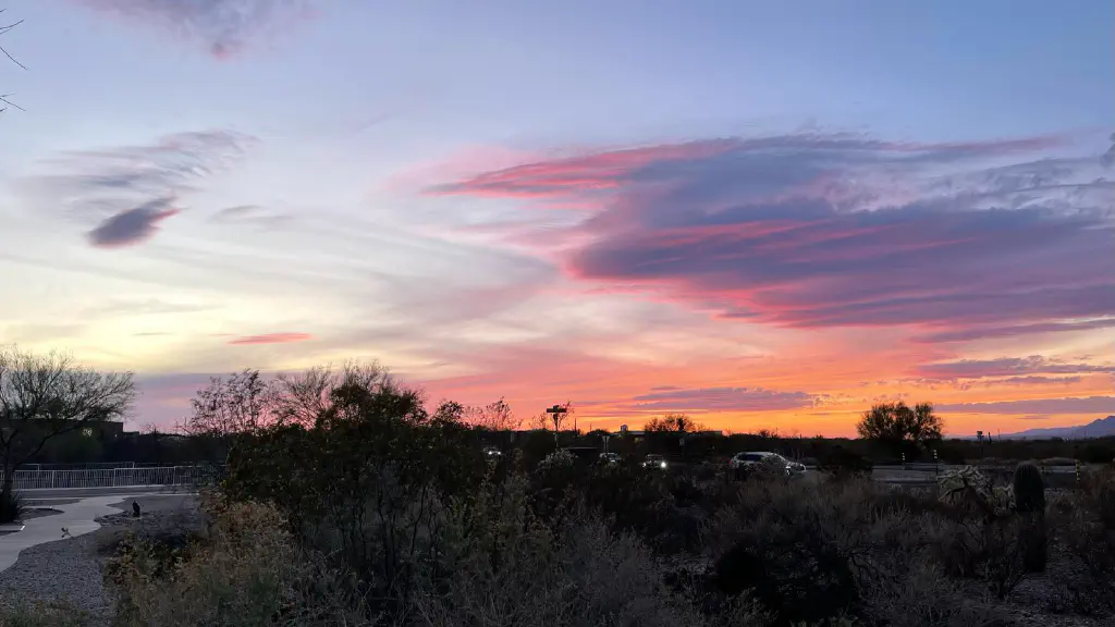 Clouds lit up orange pink and violet by freshly-set sun as the sky fades from daylight blue to evening dark