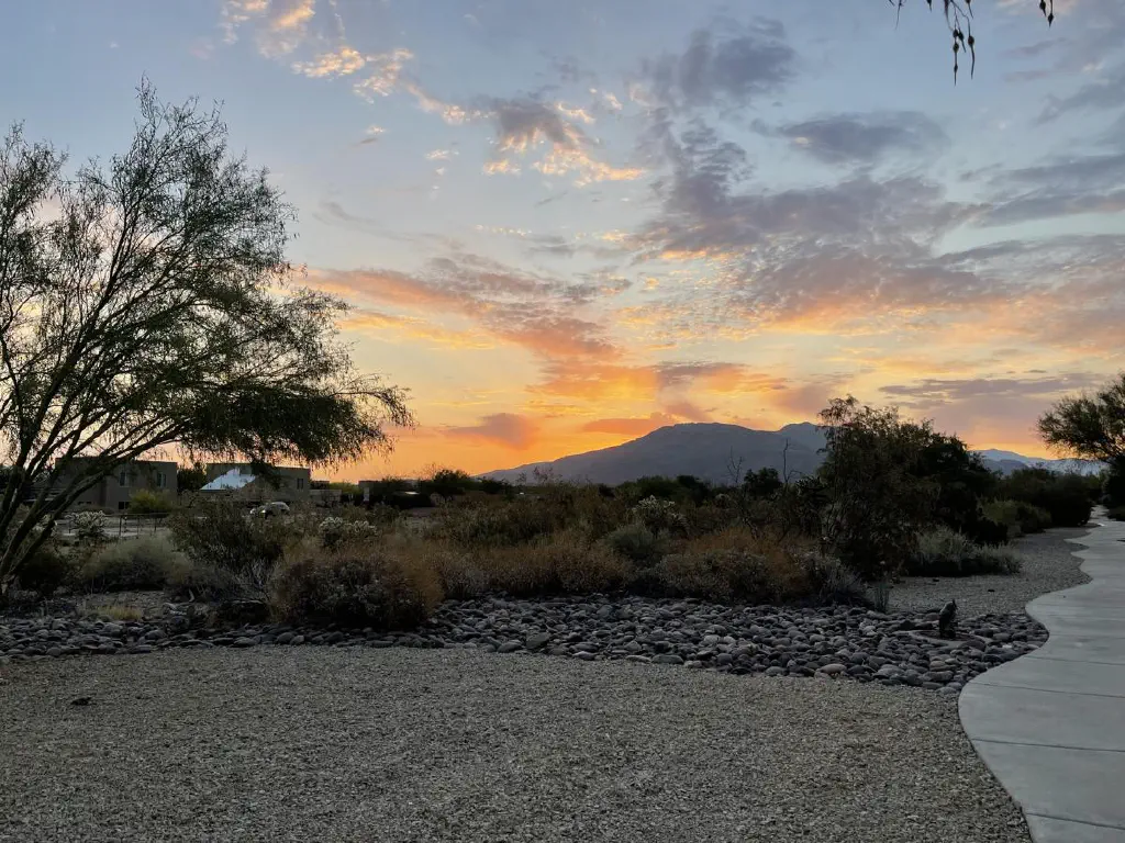 Desert sunrise, with clouds lit up in orange hues while the sun is still hidden behind a mountain