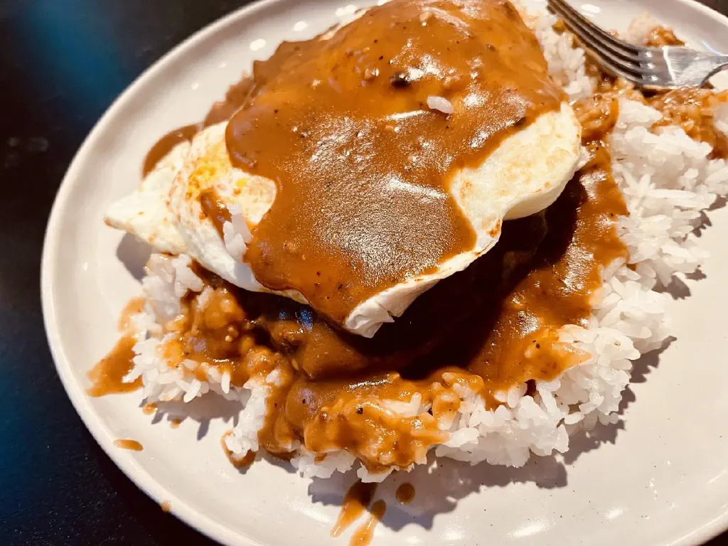 Gravy slathered over fried egg and beef patty, on a bed of rice
