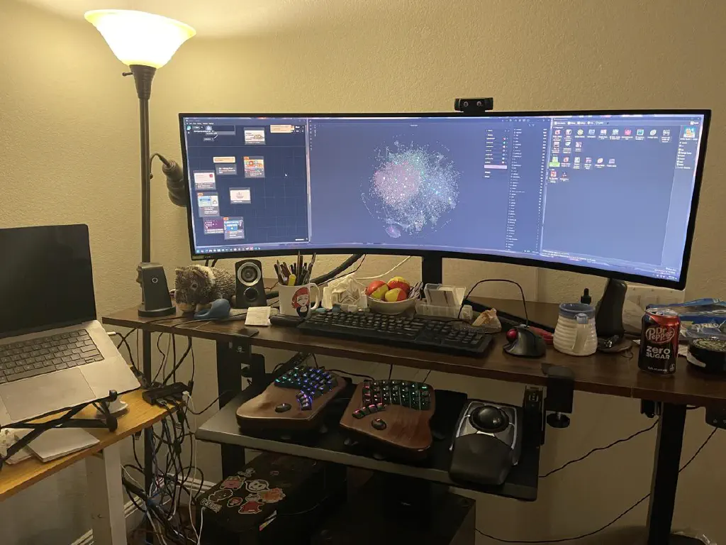 Ultra wide monitor with two keyboard + trackpad pairs beneath it, and laptop on a stand next to everything 