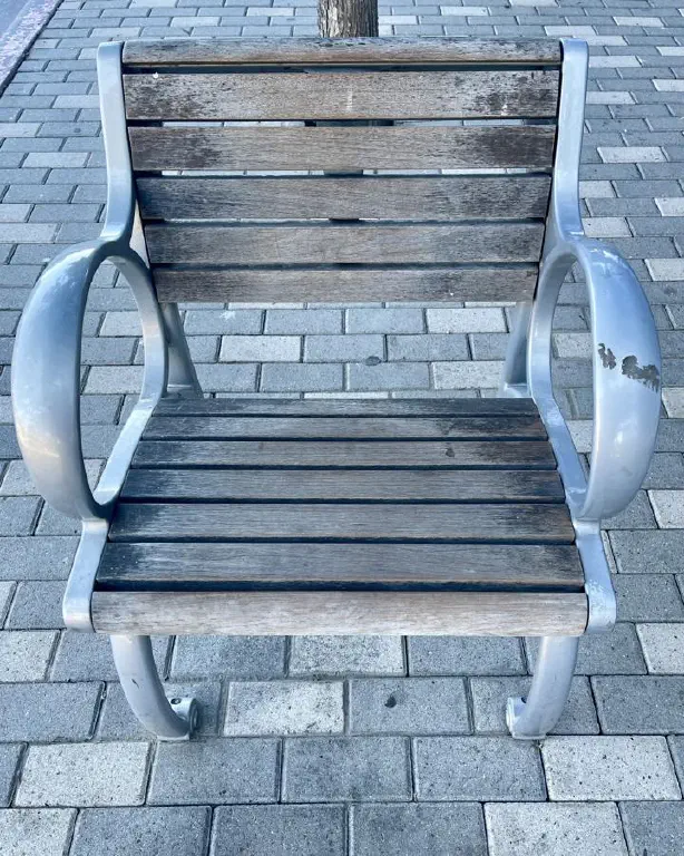 A park bench with wood slats and metal armrests, exactly wide enough to fit one average adult with excellent posture