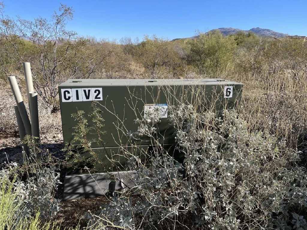 Electrical transformer box in a field, labeled “CIV 2” on one corner and “6” on another corner.