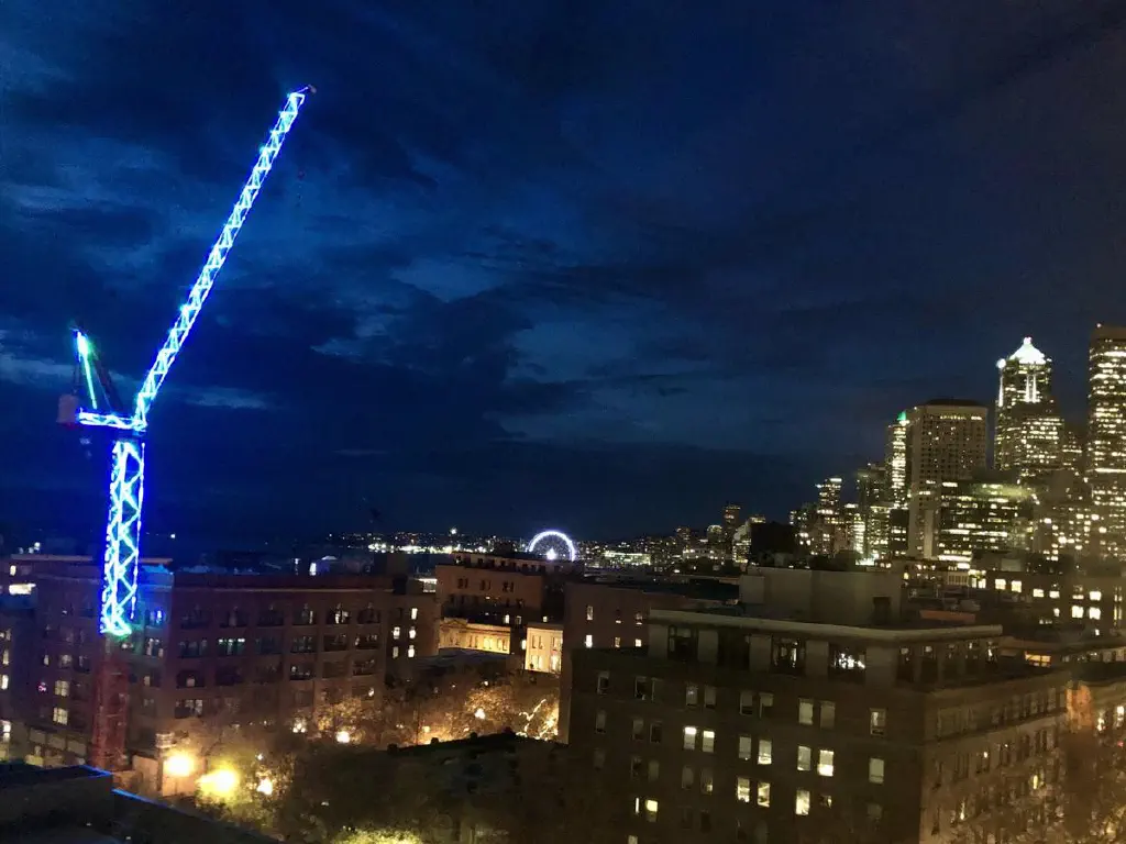 Construction crane with blue and green decorative lights against evening skyline