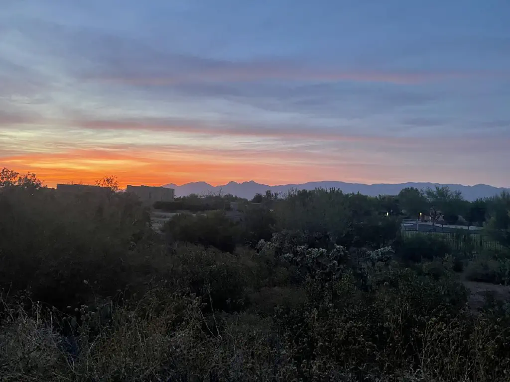 A thin line of reddish clouds under an darkening sky with mountains nearby