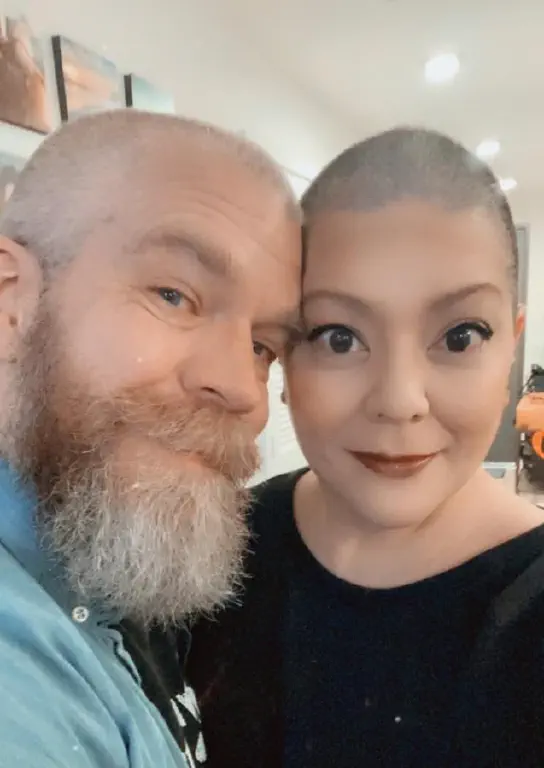 Man and woman with stubbly scalps nuzzling forehead sides for the camera