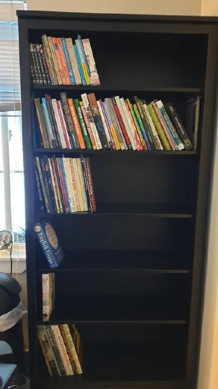 Black bookshelf about 2/3 full of books on knitting, art, and cooking