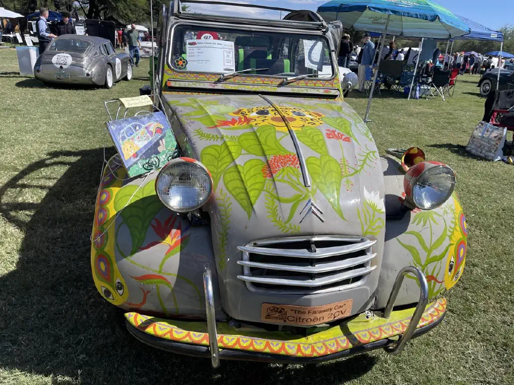 Citroen car with lots of happy painting on it; a children’s book I spire by the car rests on top of