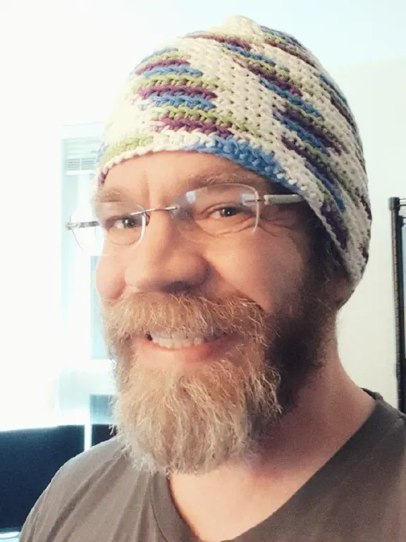 Happy bearded guy wearing bright yarn hat. 