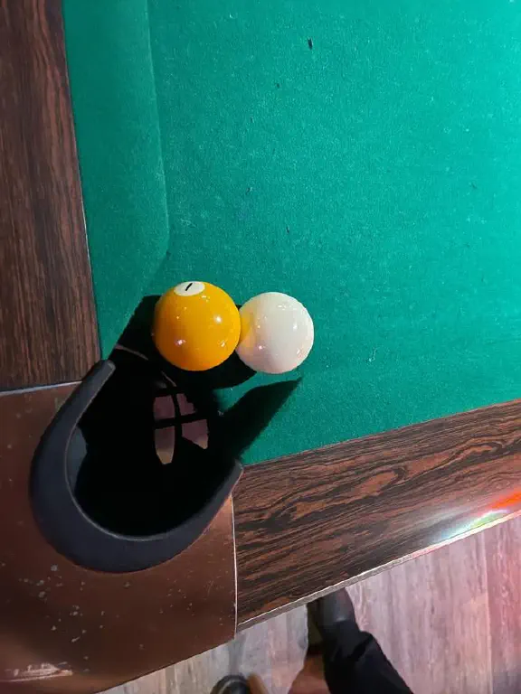 Overhead view of a pool table, with the cue ball and the 1 ball resting together on the very edge of a corner pocket 
