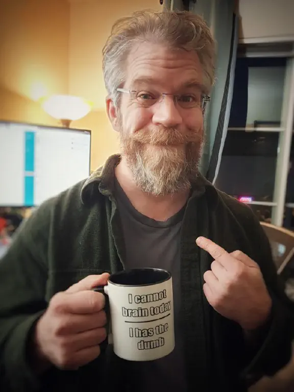 Tired beardy guy holding coffee cup that reads &ldquo;I cannot brain today — I has the dumb&rdquo;
