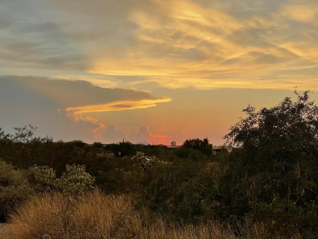 One end of the very large anvil cloud, edges draped pink and red by a setting sun