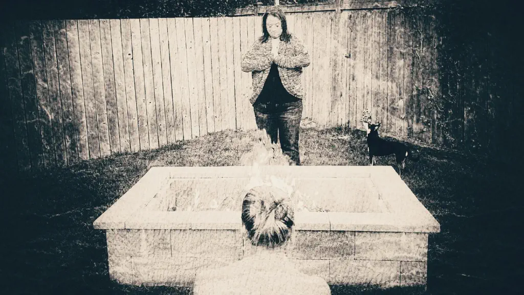 Black and white photo of women around a fire with a small curious dog looking at them