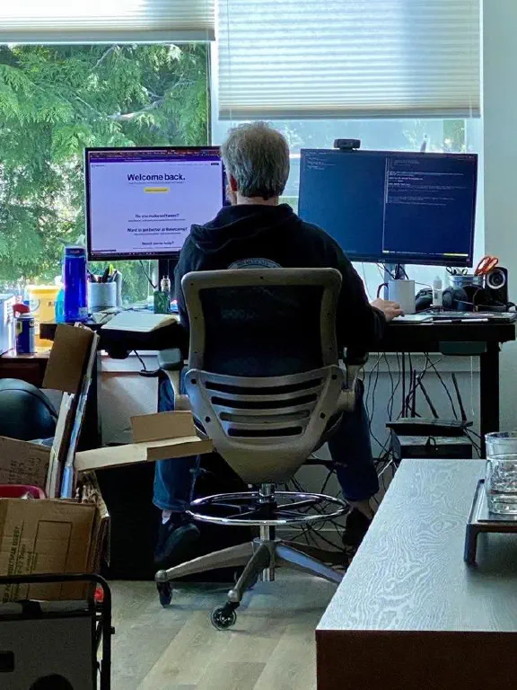person seated at desk facing away from camera in front of two monitors