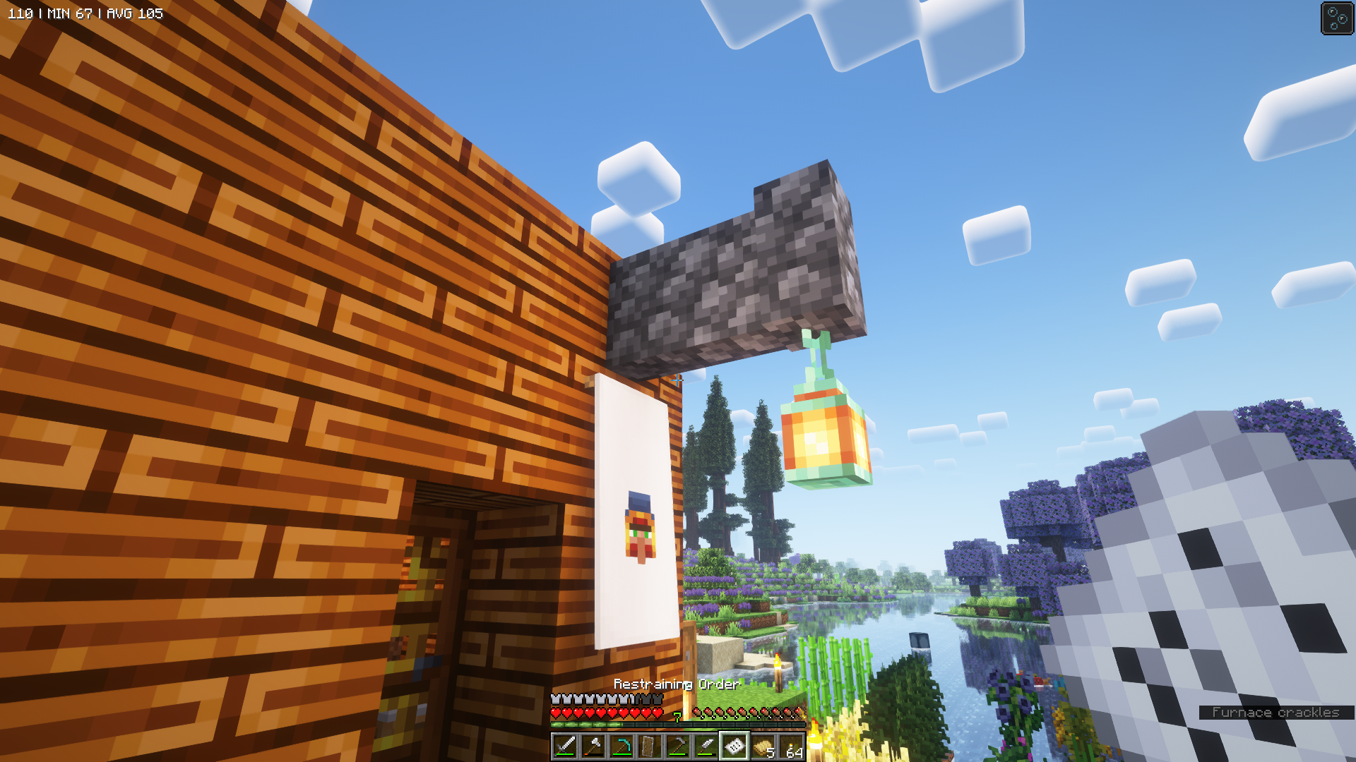 Next to the door of a Minecraft house, a copper lantern illuminates a banner with an image of the wandering trader’s face; the player is holding a piece of paper note, with inventory help text indicating this paper is a restraining order