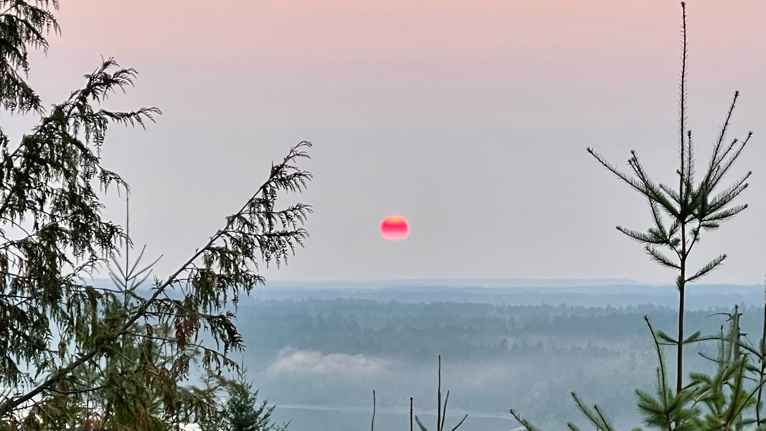 Very red sun rising over wooded hills. 