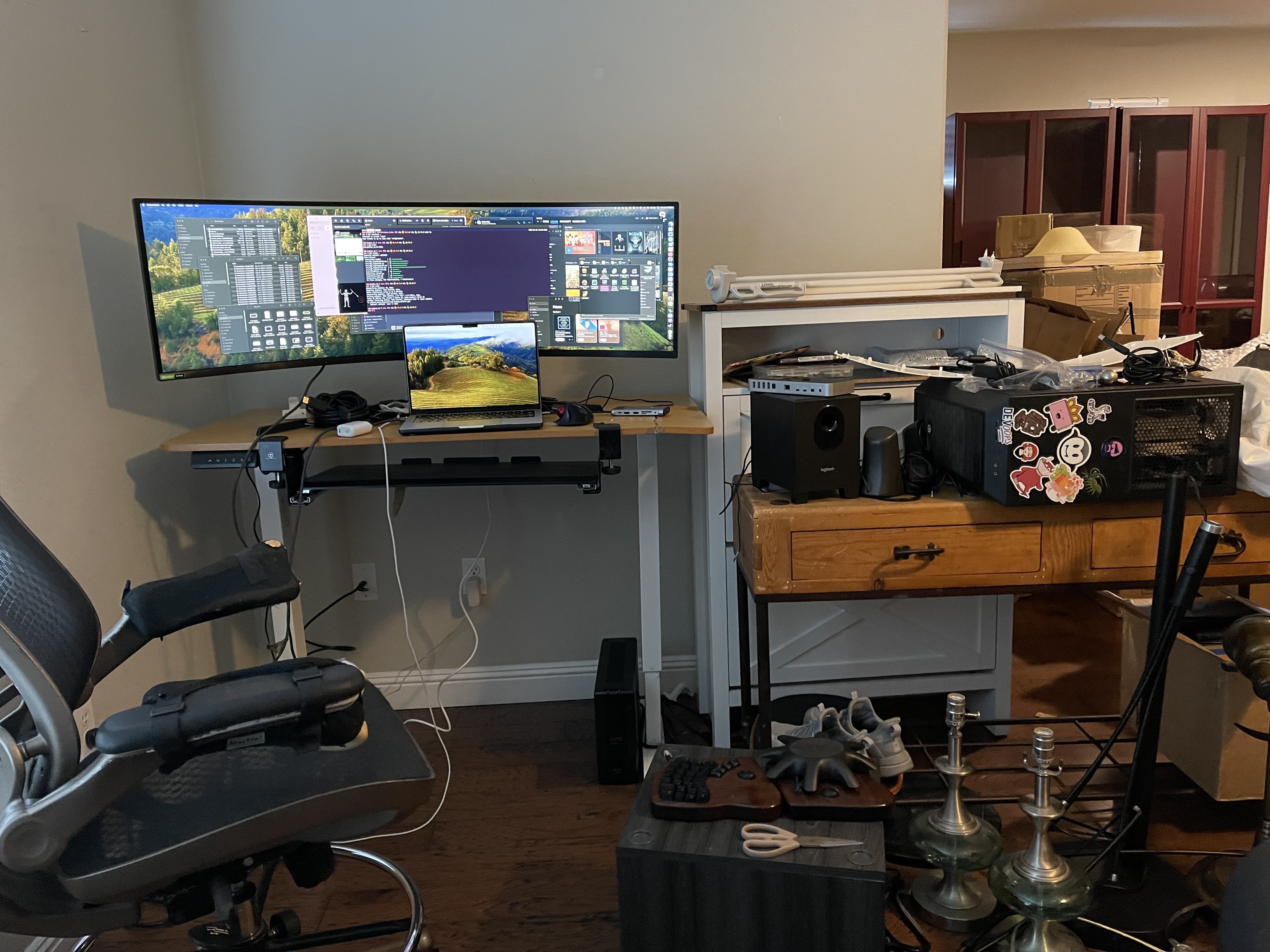 Desktop workspace in disarray, with laptop display extended to an ultrawide monitor, and a PC tower nearby on its side. 