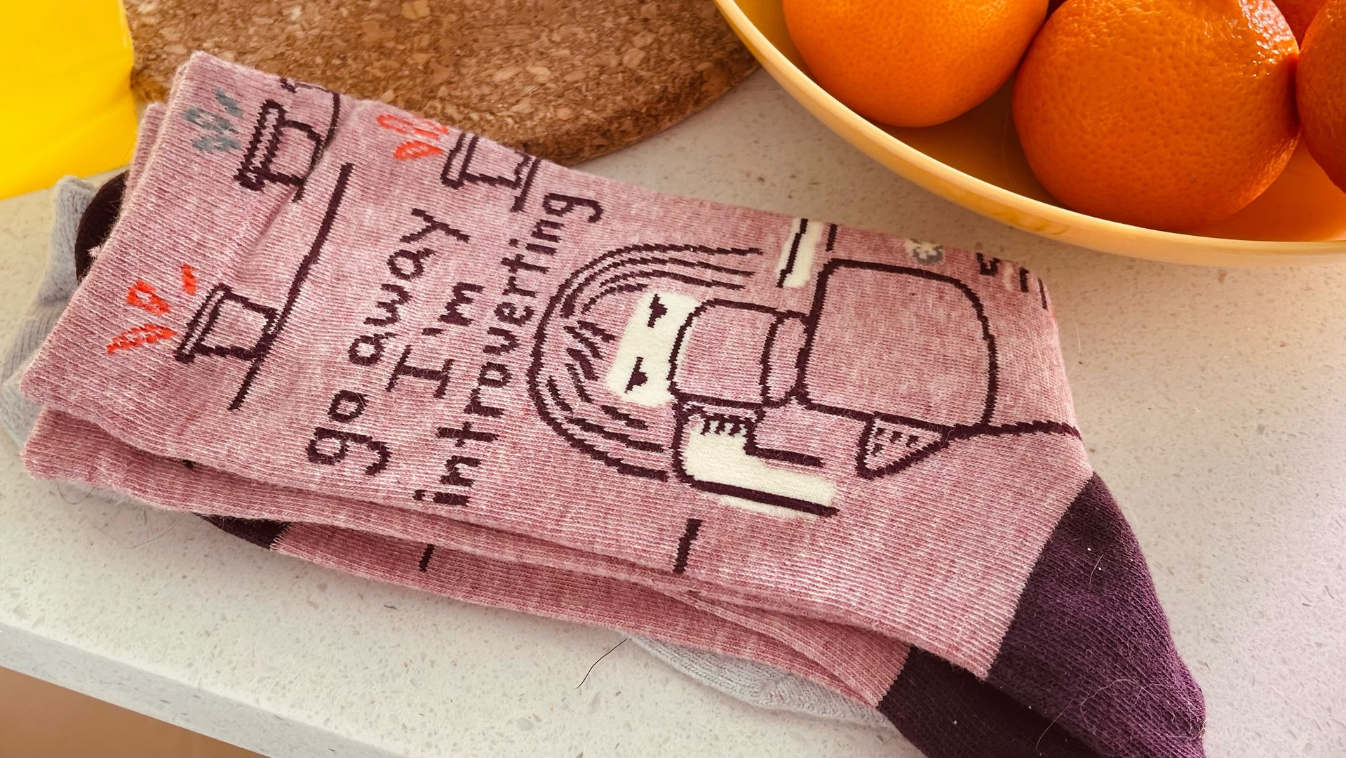 Pink socks with text “go away I’m introverting” and scowling face obscured by coffee cup