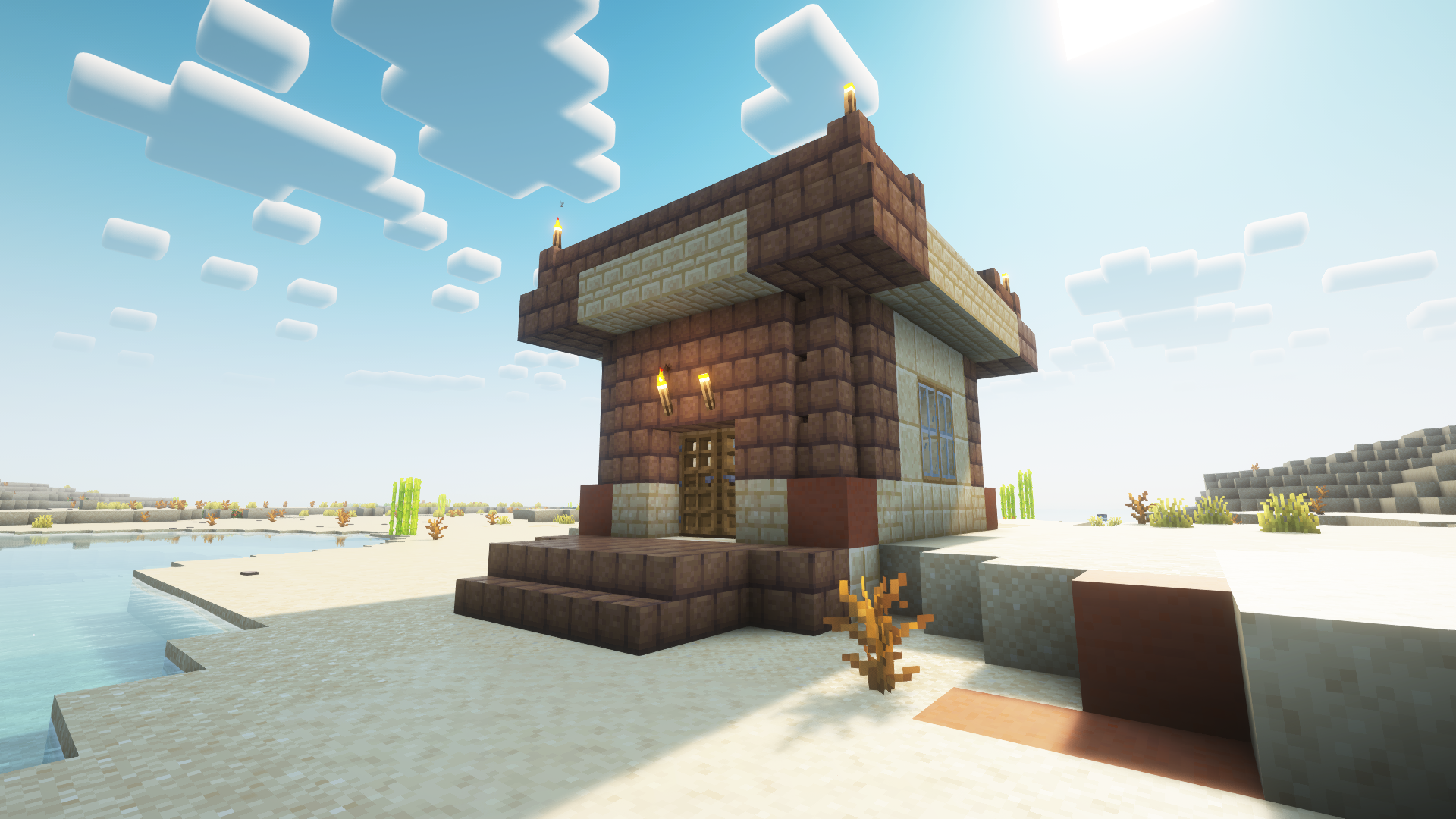Blocky house in desert near water; the house is made of sandstone and mud bricks, with some terracotta for color