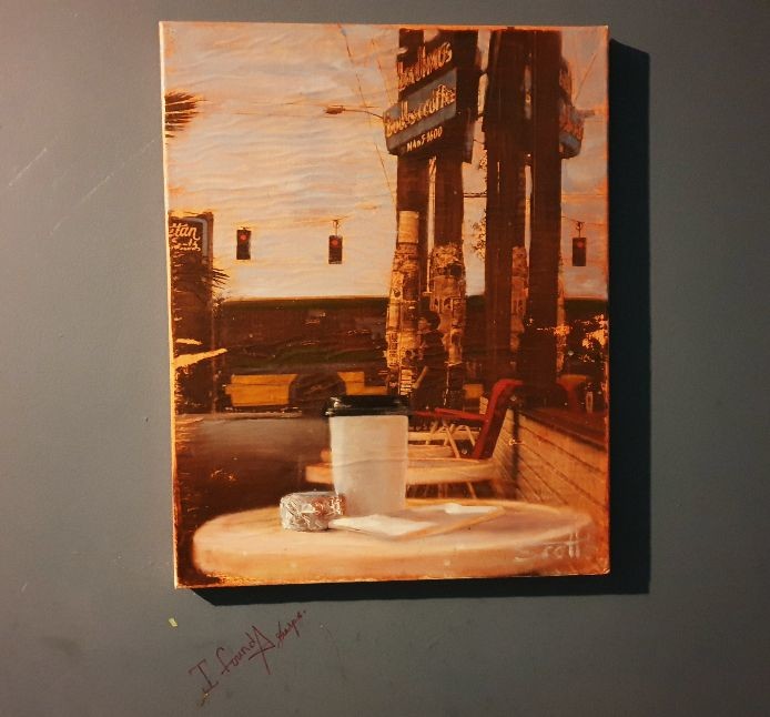 painting of coffee cup on outdoor cafe table with traffic lights in background; under painting “I found a sharpie.” is written on wall