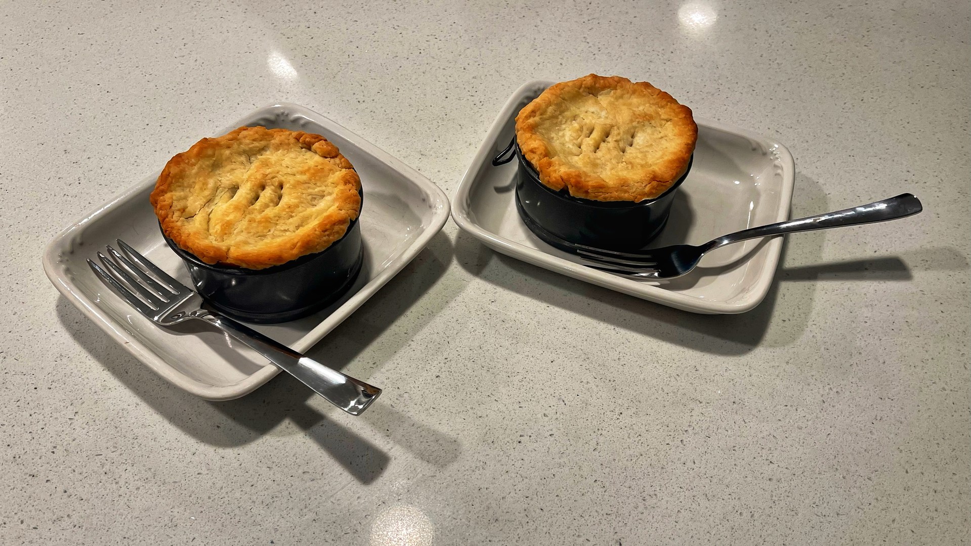 Two small pie dishes on plates with forks. 