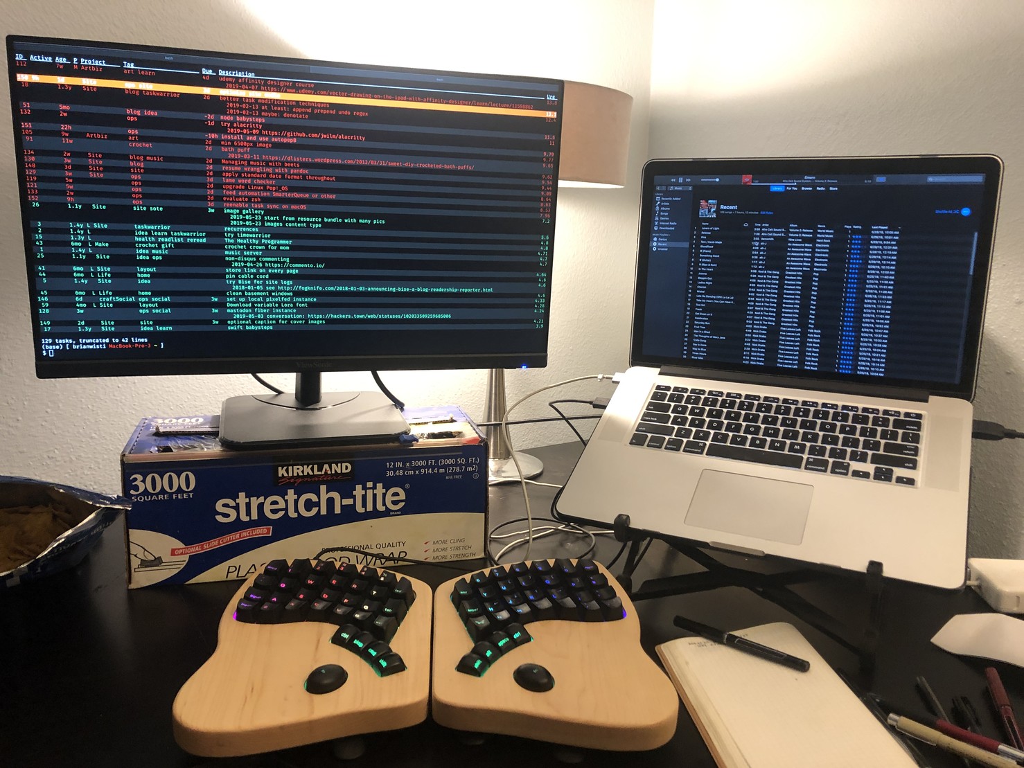 Laptop on roost stand showing iTunes, model 01 fancy keyboard, next to monitor with full screen terminal. 